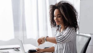 Image of a woman siting in her office, looking at her wristwatch