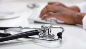 Close up image of a stethoscope with a doctor's hand typing on a keyboard in the background
